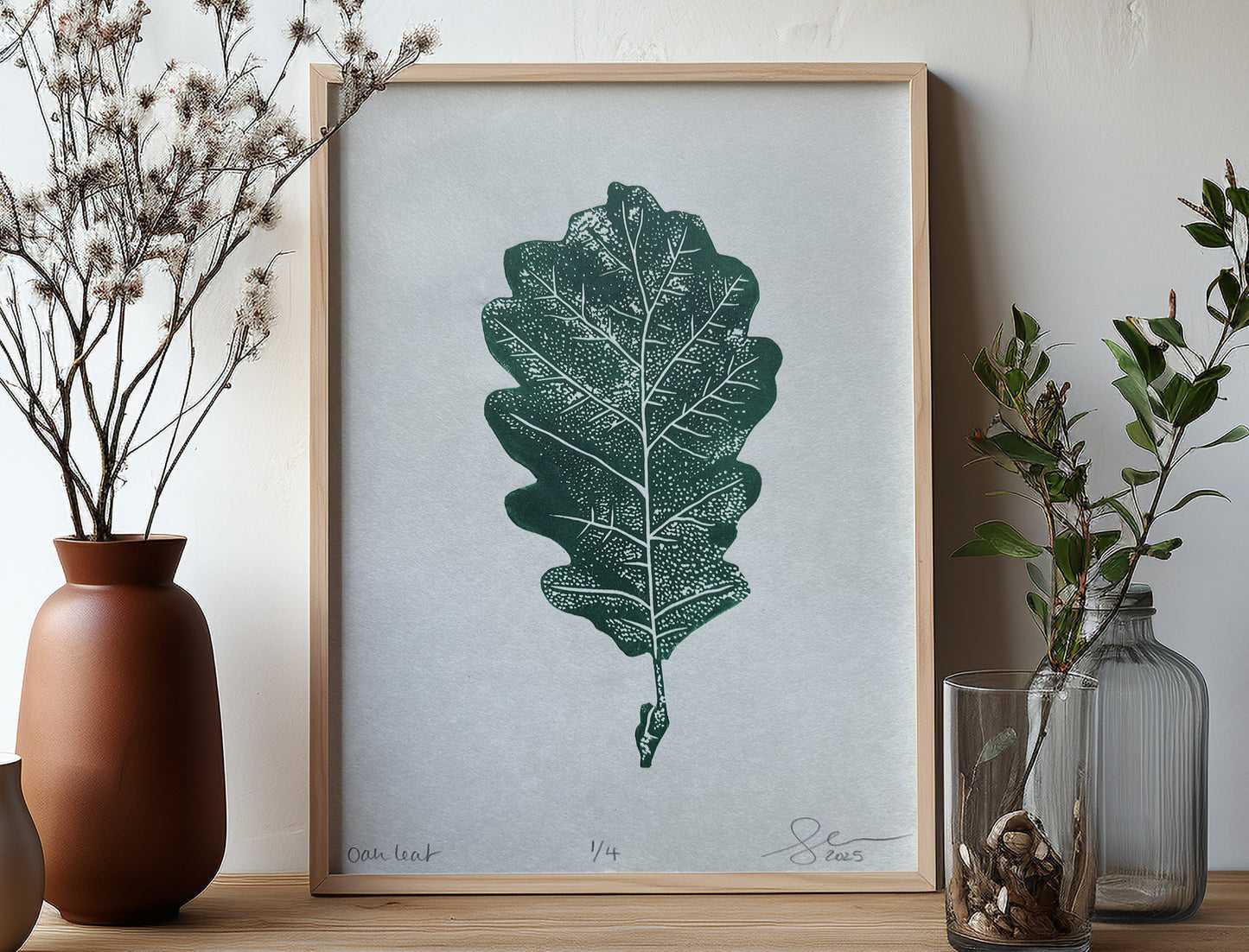 A lino print of an oak leaf in phthalo green, mocked up into a wooden frame.