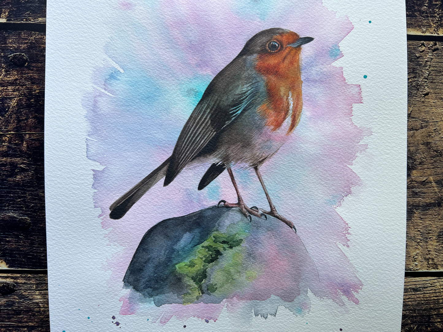 An original watercolour painting of a robin on a rock with a pink and turquoise background