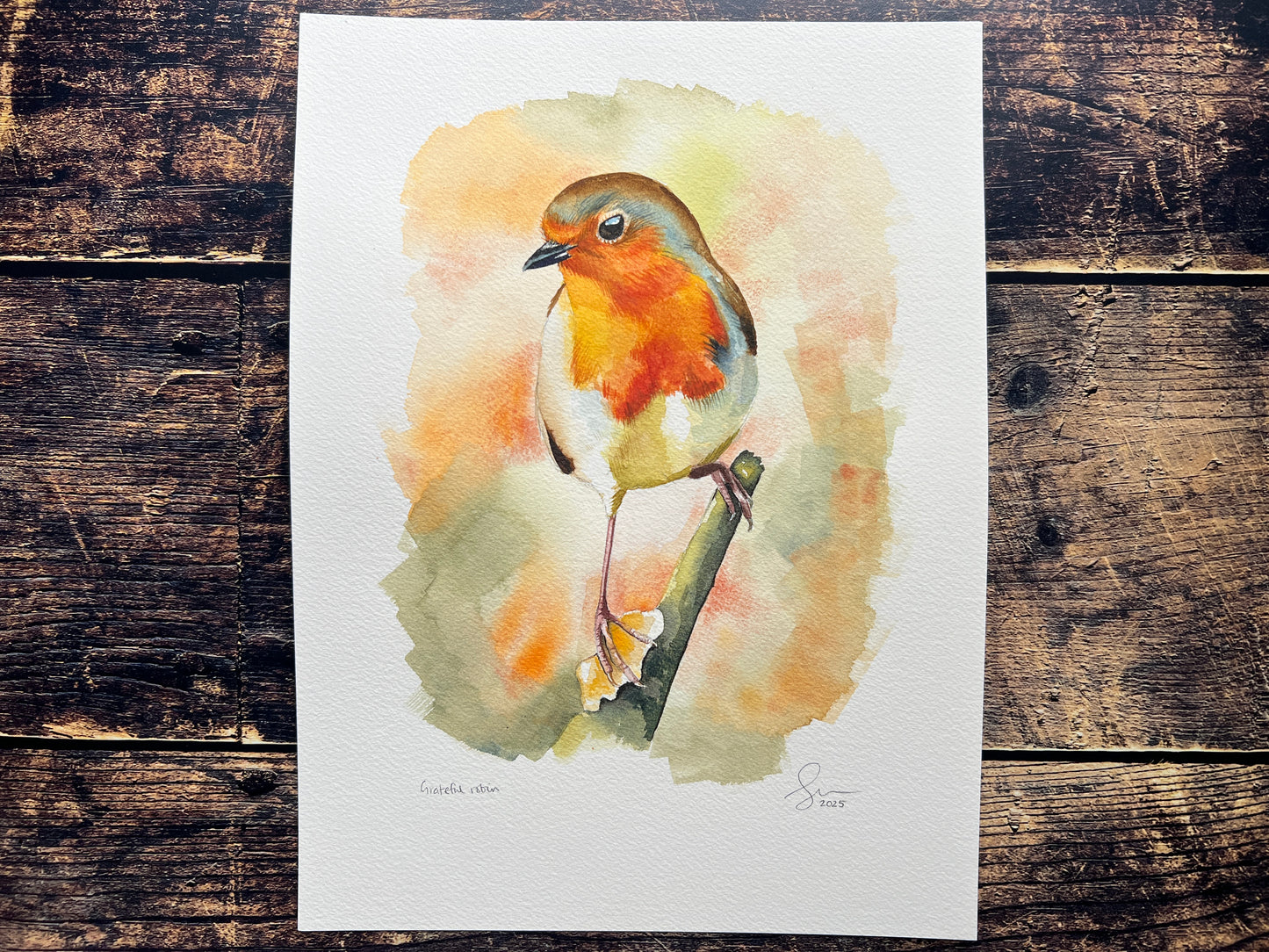 A watercolour painting of a robin, surrounded by blurry autumnal colours.