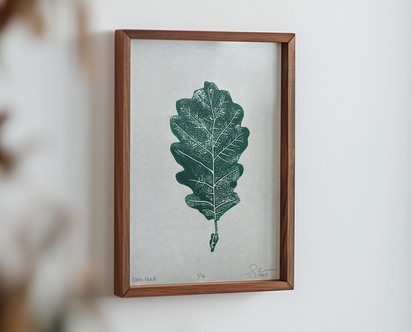 A lino print of an oak leaf in phthalo green, mocked up into a wooden frame.