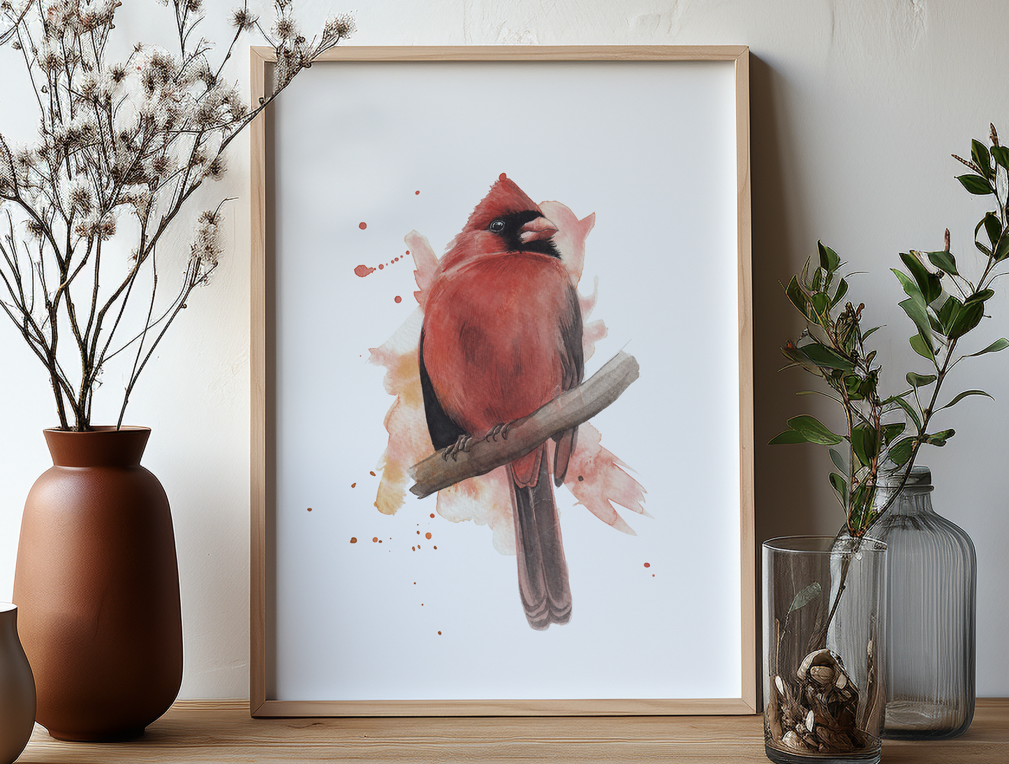 A watercolour print of a male cardinal bird, painted in an expressive way, in a frame on a shelf