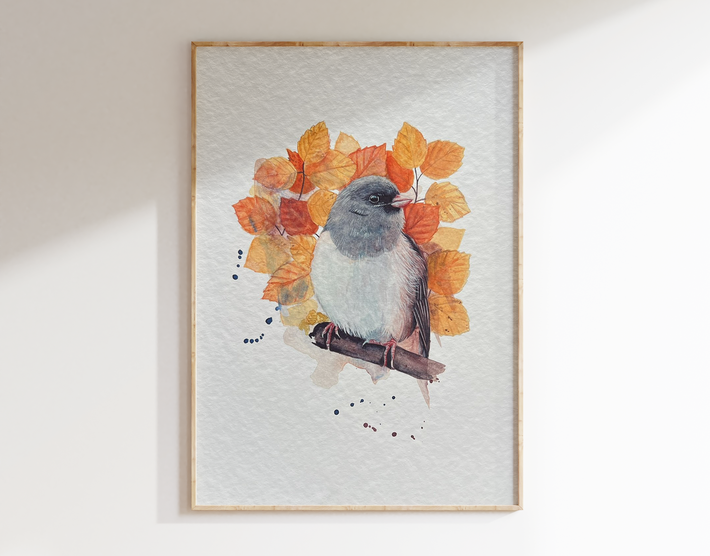 This is a watercolour print of a dark eyed junco, surrounded by autumnal coloured leaves
