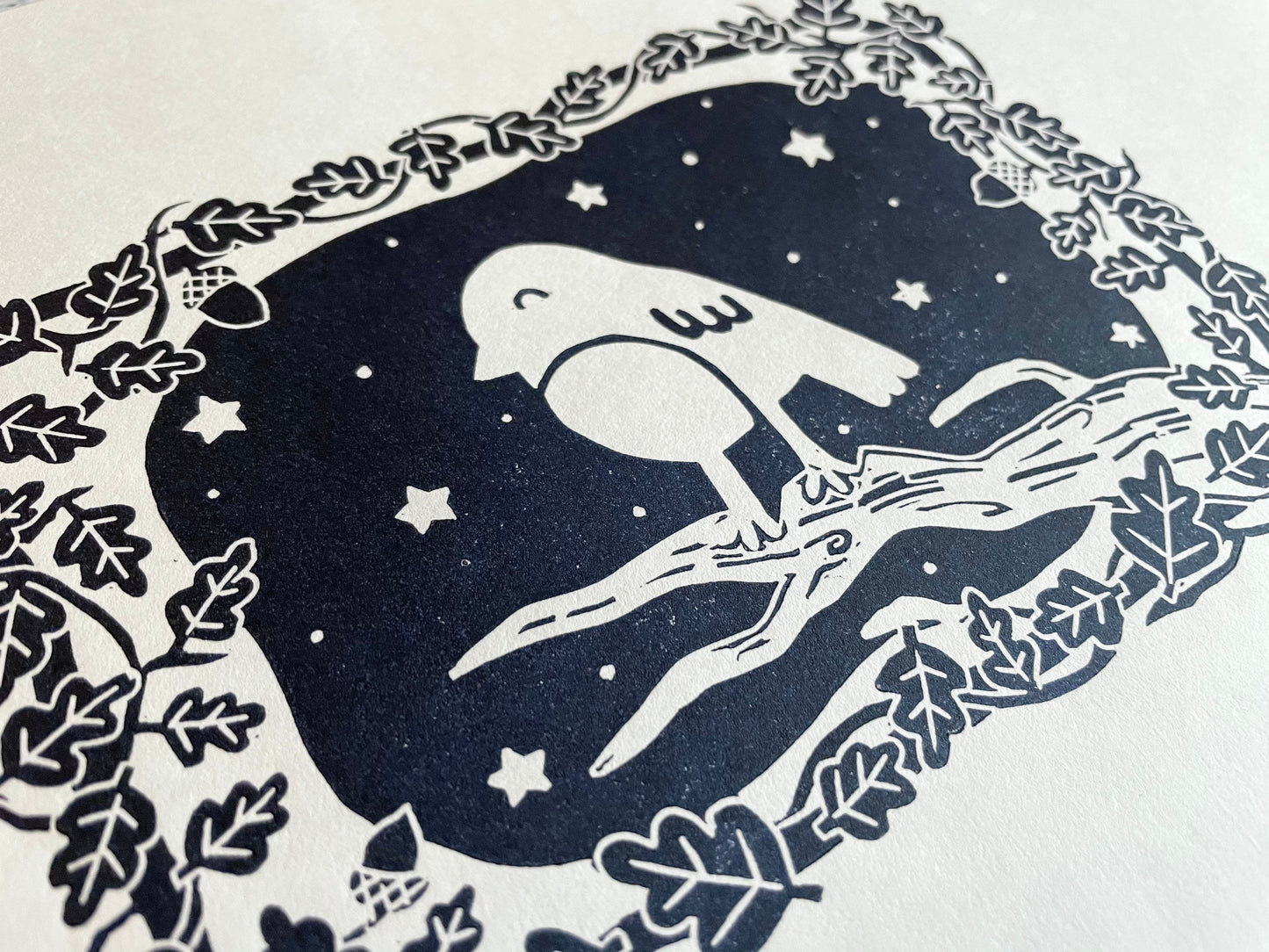 A small lino print of a robin on a tree surrounded by oak leaves and stars