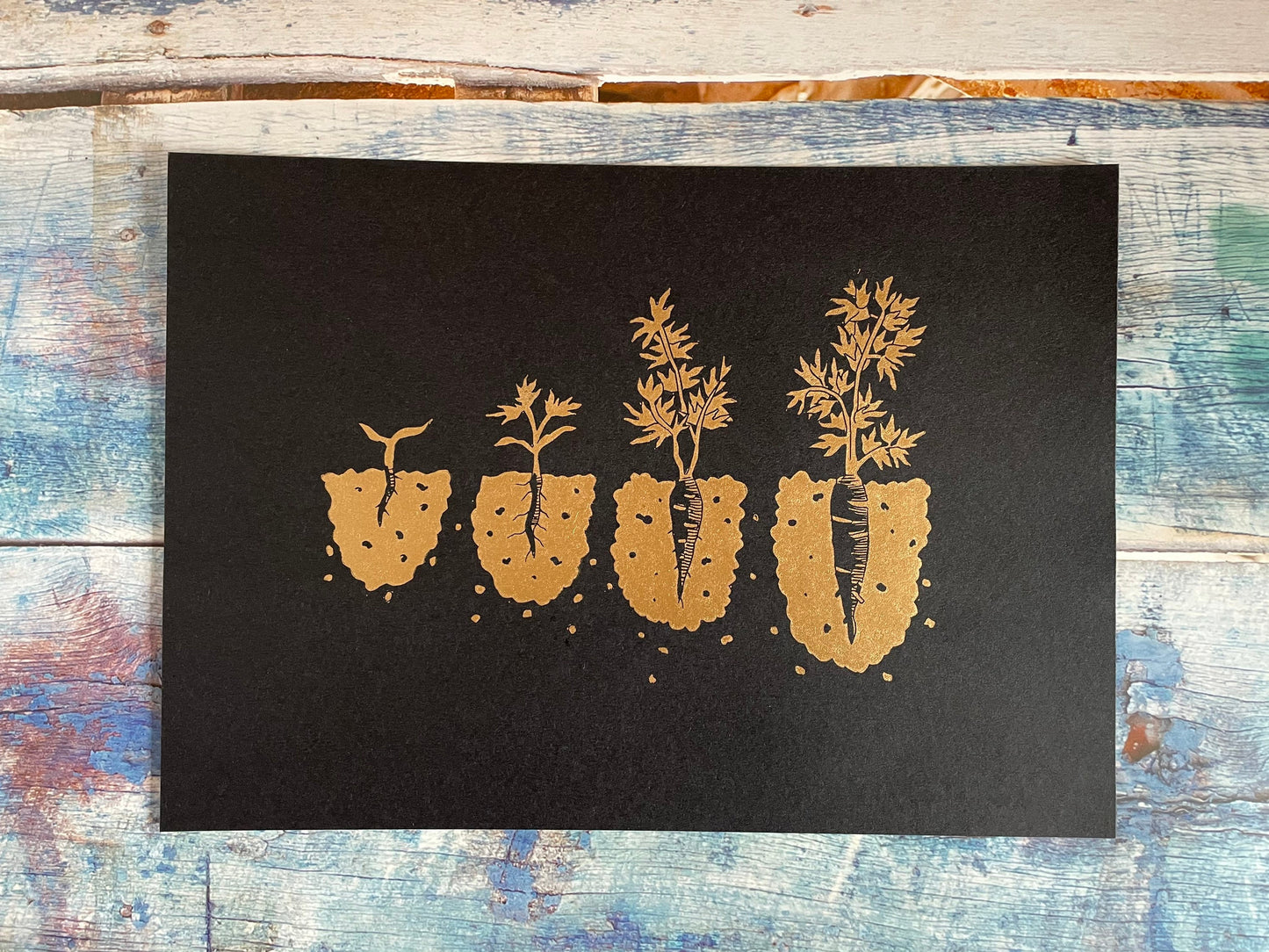 A lino print showing the different stages of a carrot growing from seedling to ready to pick in copper on black