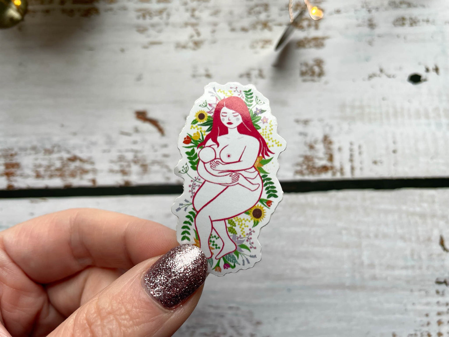 A 5cm sticker of a breastfeeding mother laying on a bed of flowers and leaves