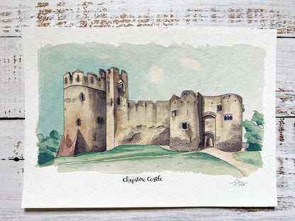 An A4 watercolour print of Chepstow Castle on a white rustic wooden background