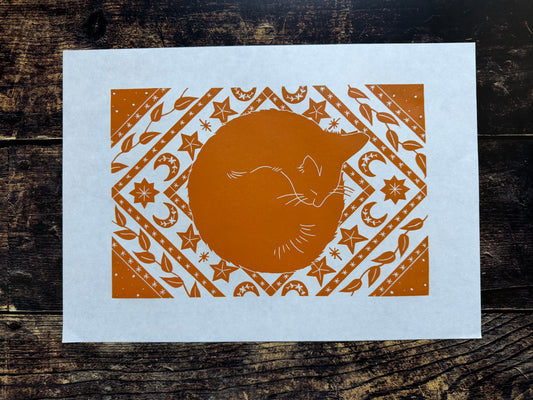 A lino print in orange of a cat sleeping on a celestial mat