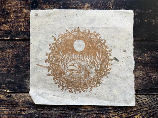 This is a lino print in gold ink of a badger sleeping in a field of wheat. It's printed slightly off centre