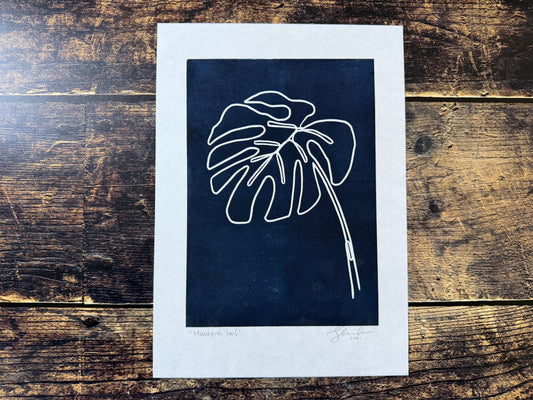 A photo of a navy blue lino print of a single monstera leaf
