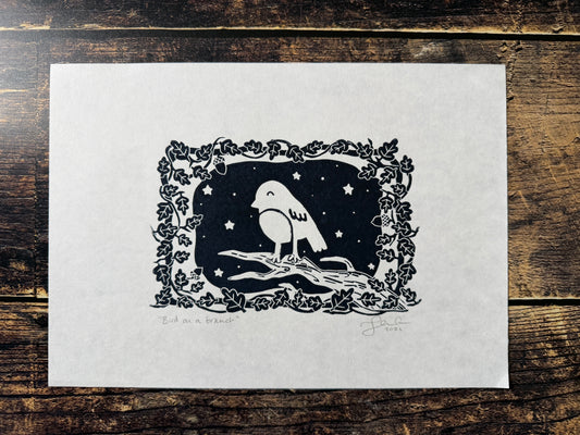 A photo of a lino print of a bird on a branch, sleeping with a starry sky behind