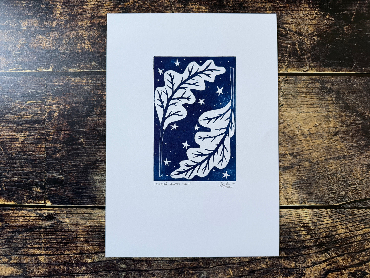 A lino print featuring oak leaves with a night sky behind