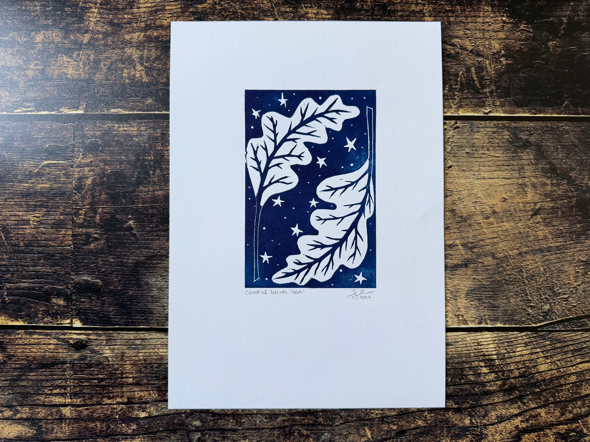 A lino print featuring oak leaves with a night sky behind