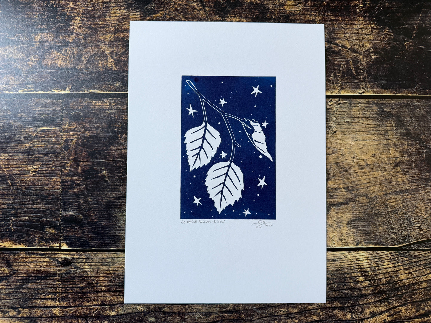A lino print featuring birch leaves with a night sky behind
