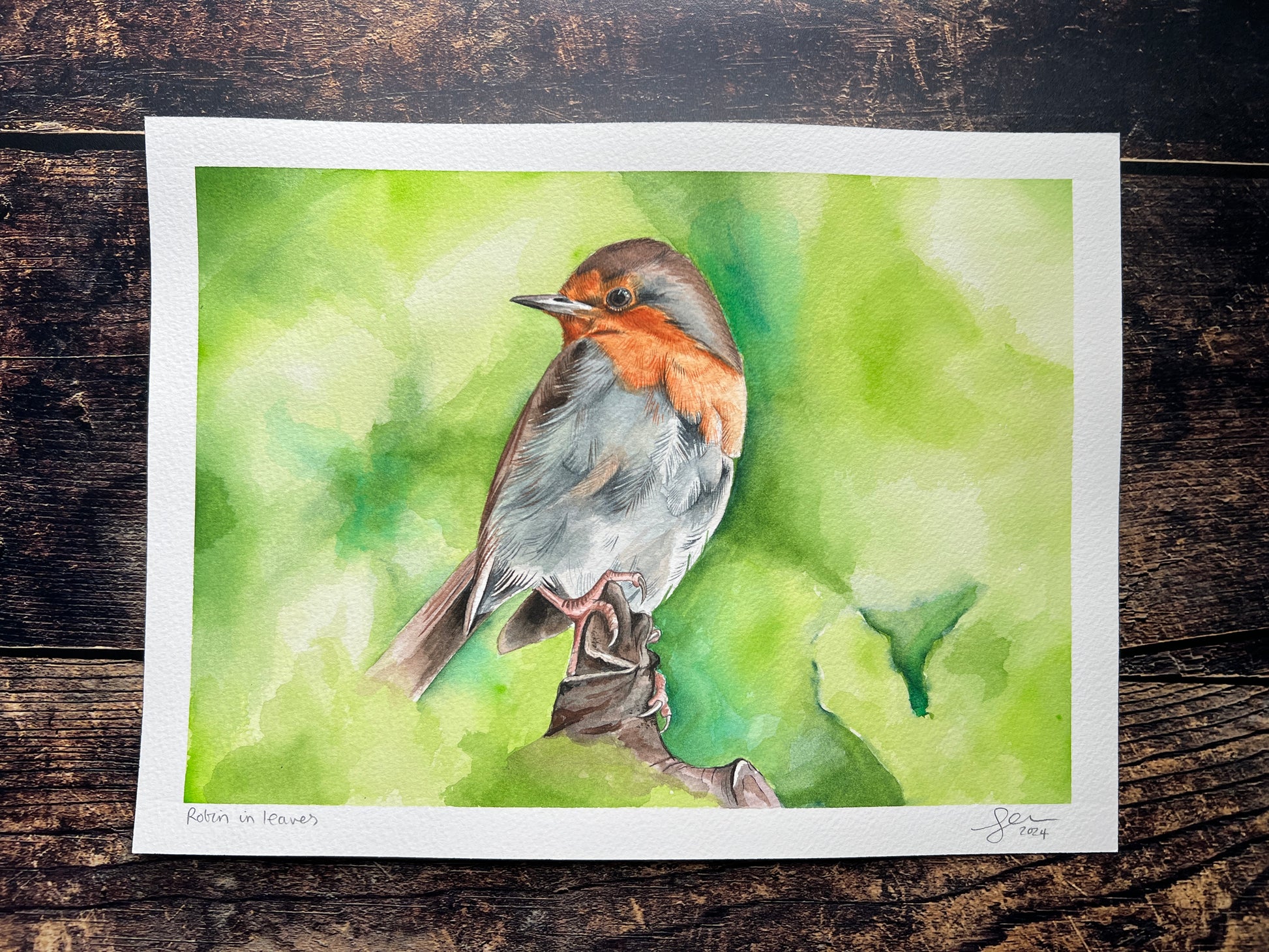 Watercolor painting of a bird on a green background, displayed on a wooden surface.