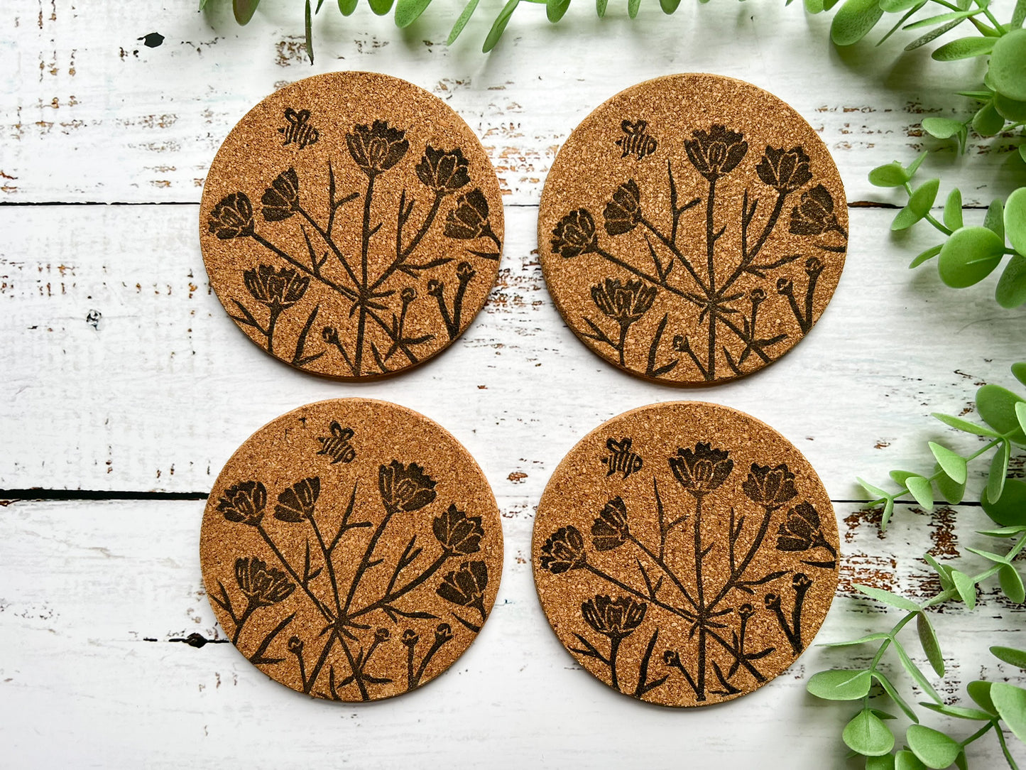 A set of four natural cork coasters with a black floral motif including a bee