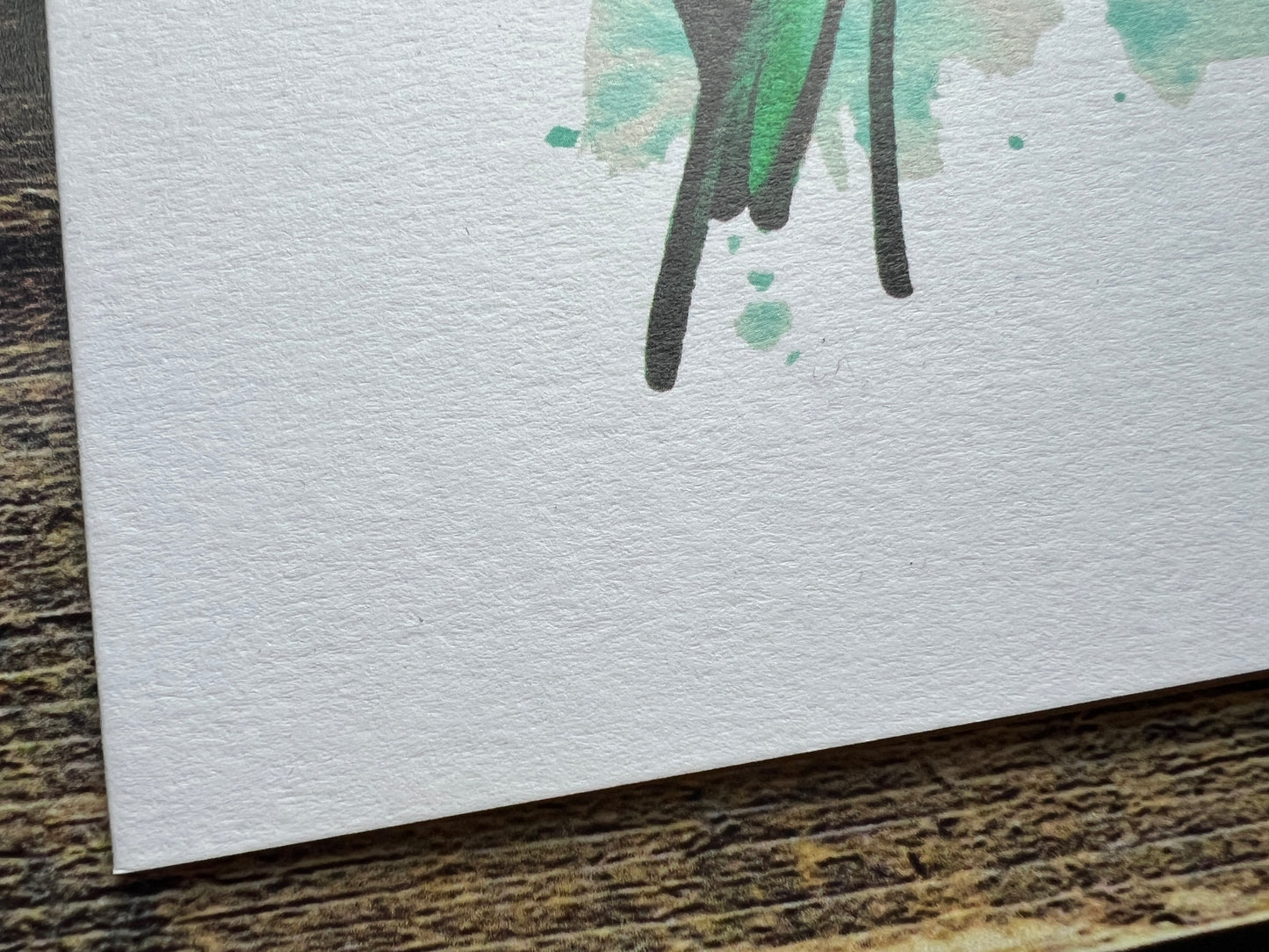 Close-up of a textured white card with watercolor paint splashes on a wooden surface