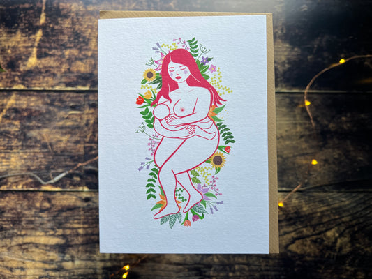 Greeting card with a stylized illustration of a woman holding a baby surrounded by flowers on a wooden surface.