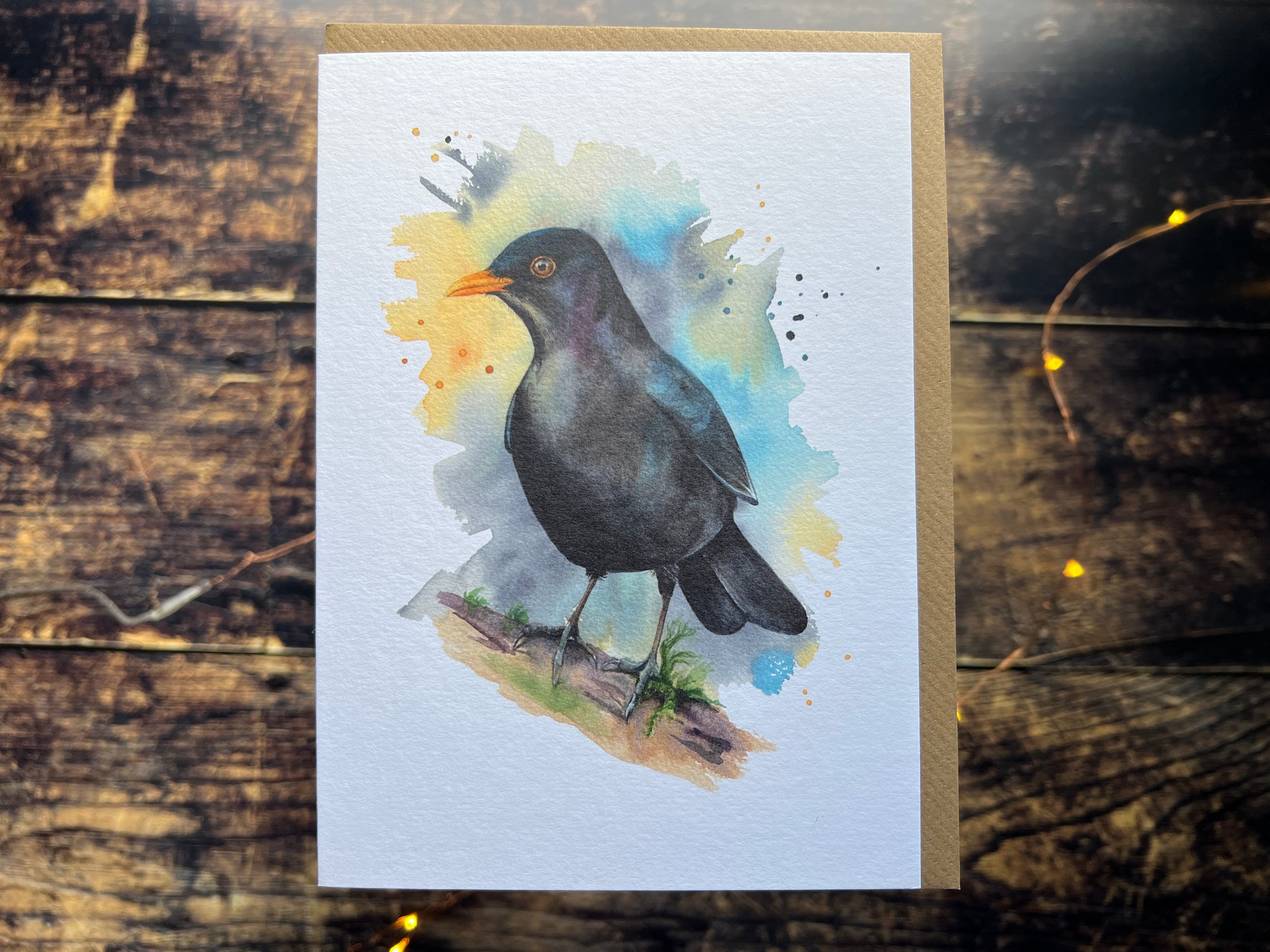 A greetings card with a watercolour blackbird on the front, surrounded by a colourwash and splashes (yellow, turquoise and phthalo blue).