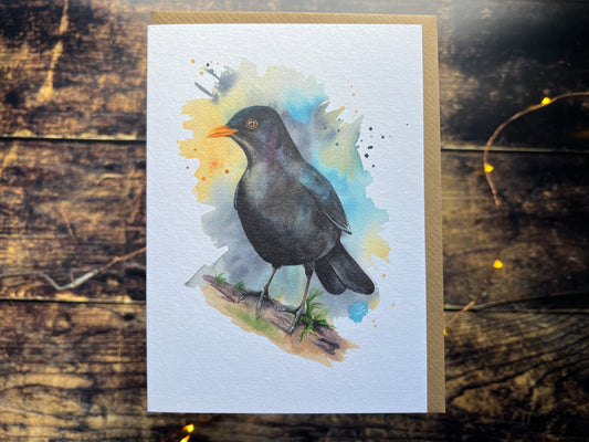 A greetings card with a watercolour blackbird on the front, surrounded by a colourwash and splashes (yellow, turquoise and phthalo blue).