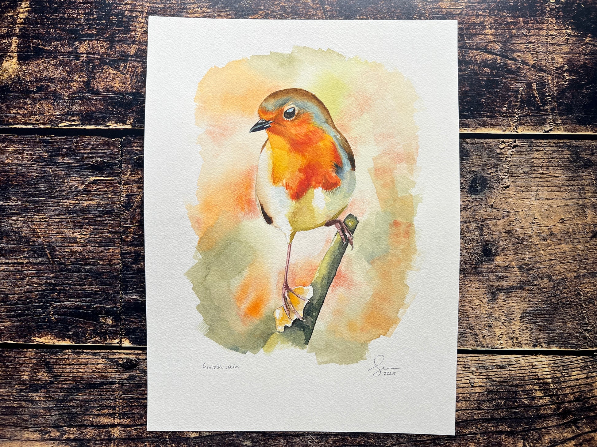 A watercolour painting of a robin, surrounded by blurry autumnal colours.