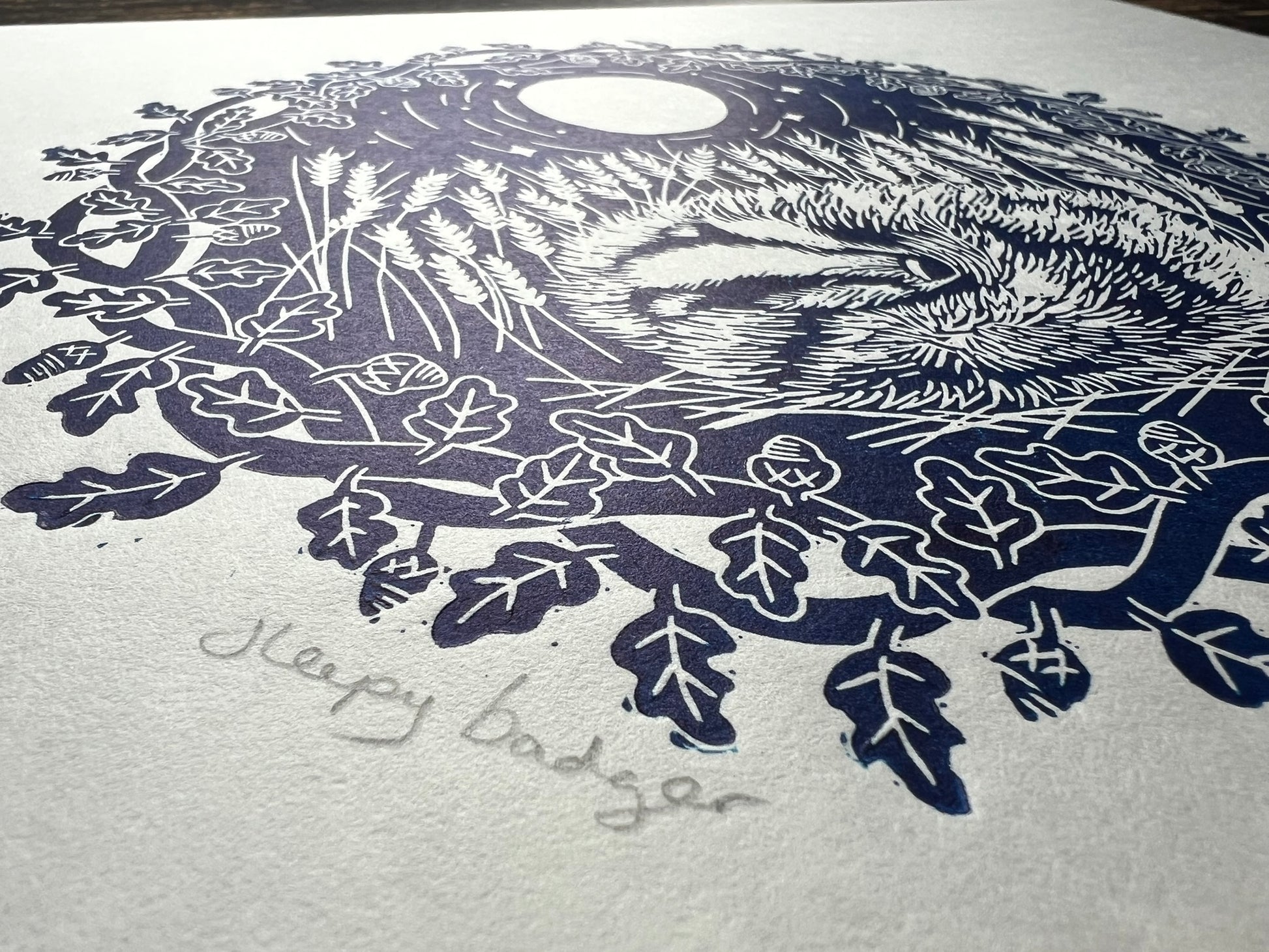 A handprinted linoprint of a badger sleeping in a field of wheat.