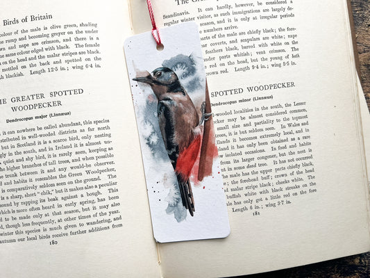 A photo of a bookmark of a great spotted woodpecker watercolour, photographed on an open book