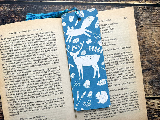 A blue bookmark with white woodland animals on, photographed on an open book