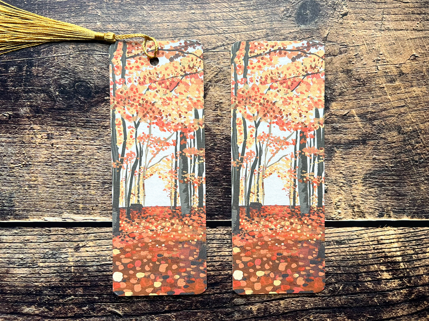 A photo of two autumnal woodland bookmarks, one has a golden tassel and one has no tassel.