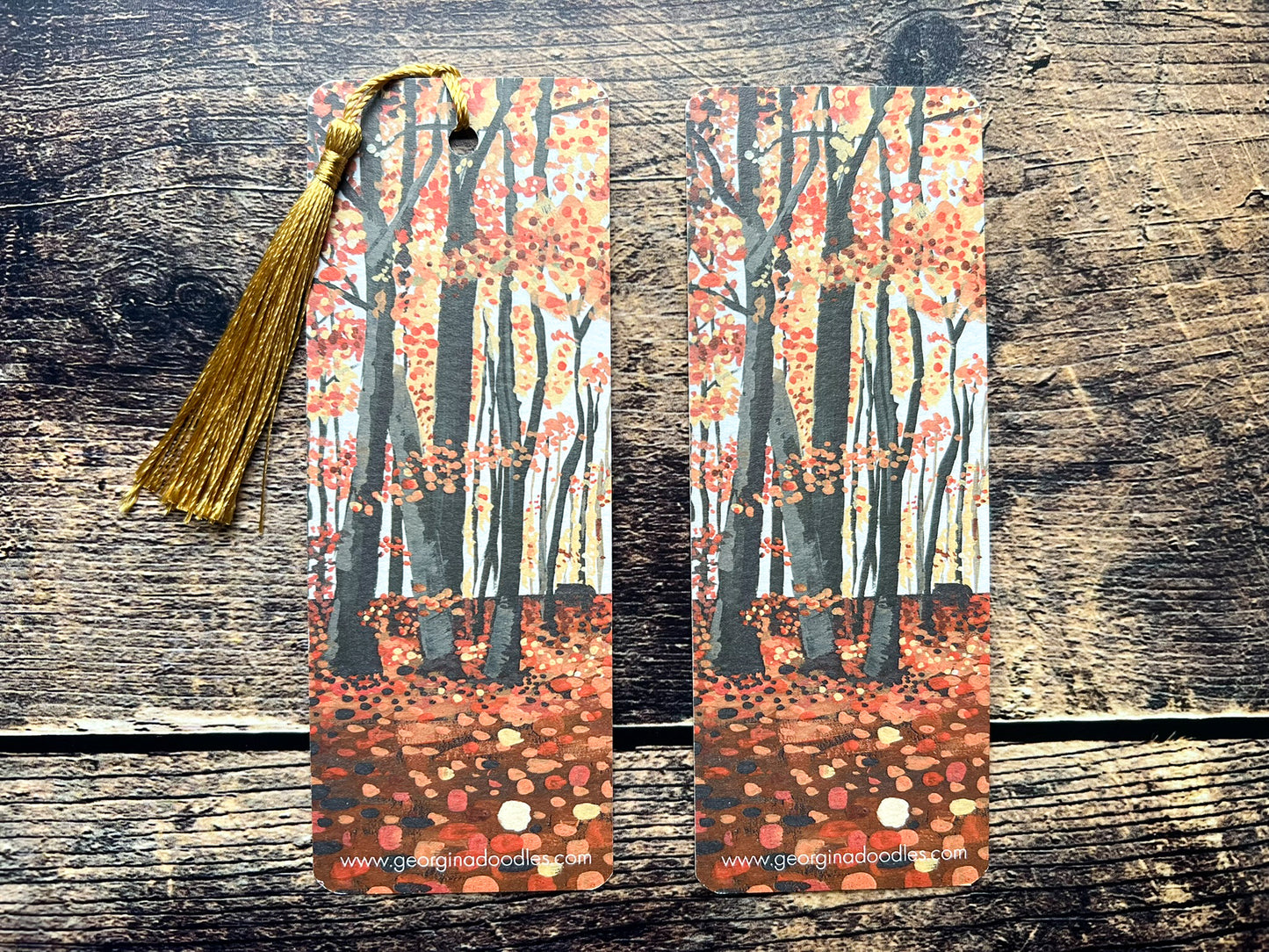 A photo of two autumnal woodland bookmarks, one has a golden tassel and one has no tassel.