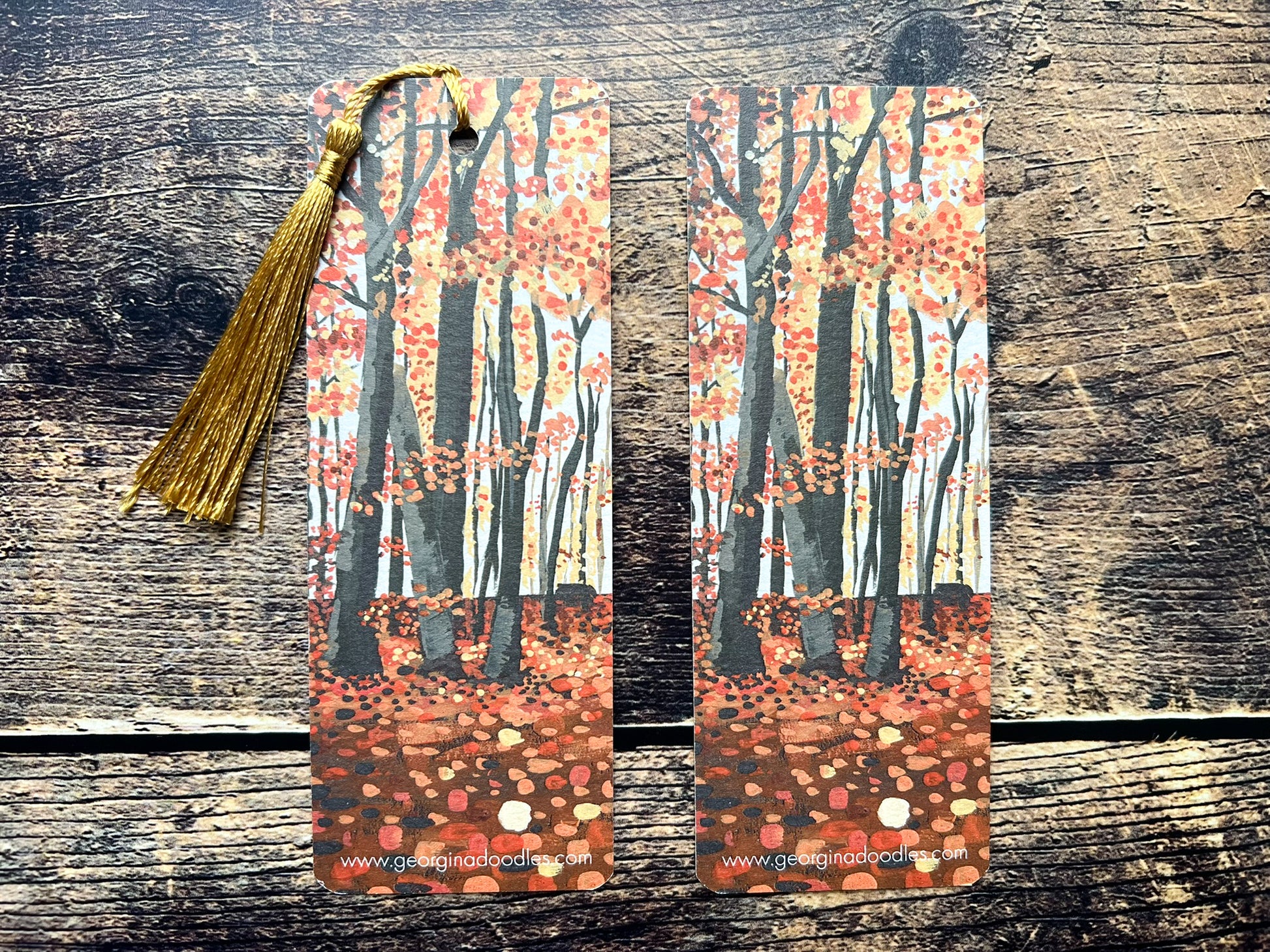 A photo of two autumnal woodland bookmarks, one has a golden tassel and one has no tassel.