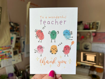 A hand holding an A6 card with six fingerprinted birds on the front. The card reads 'To a wonderful teacher, thank you'.