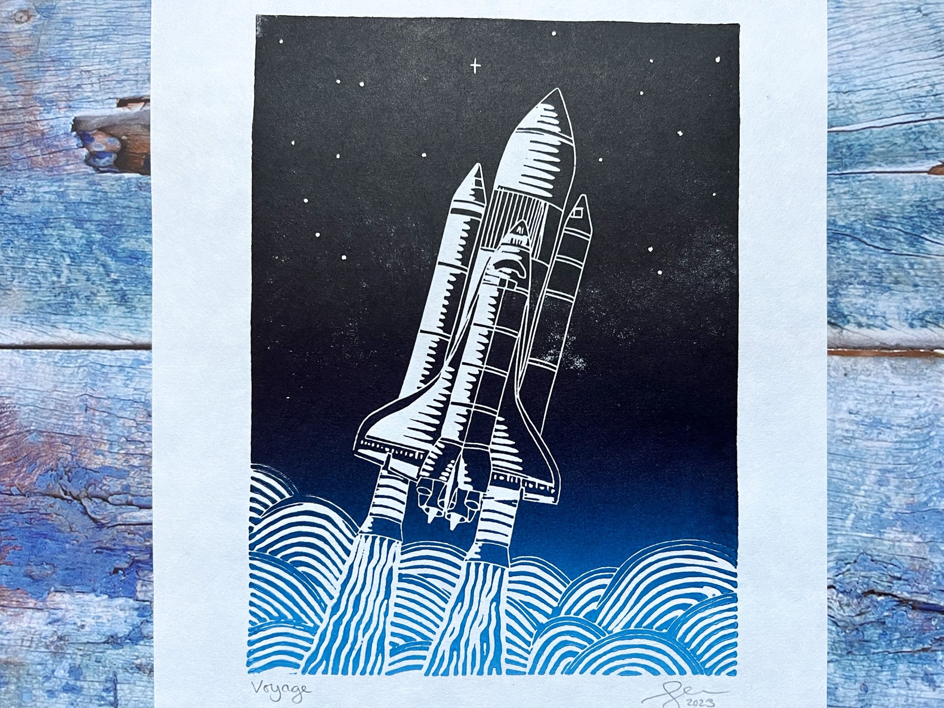 A close up of an A4 lino print with a light blue to black gradient or a space shuttled exiting earth's atmosphere