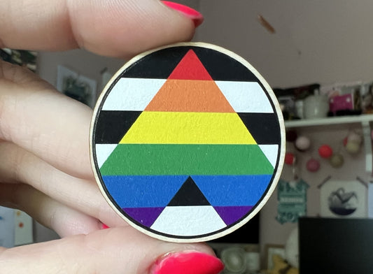 A close up of a wooden 4cm dia round pin with the Pride ally flag on