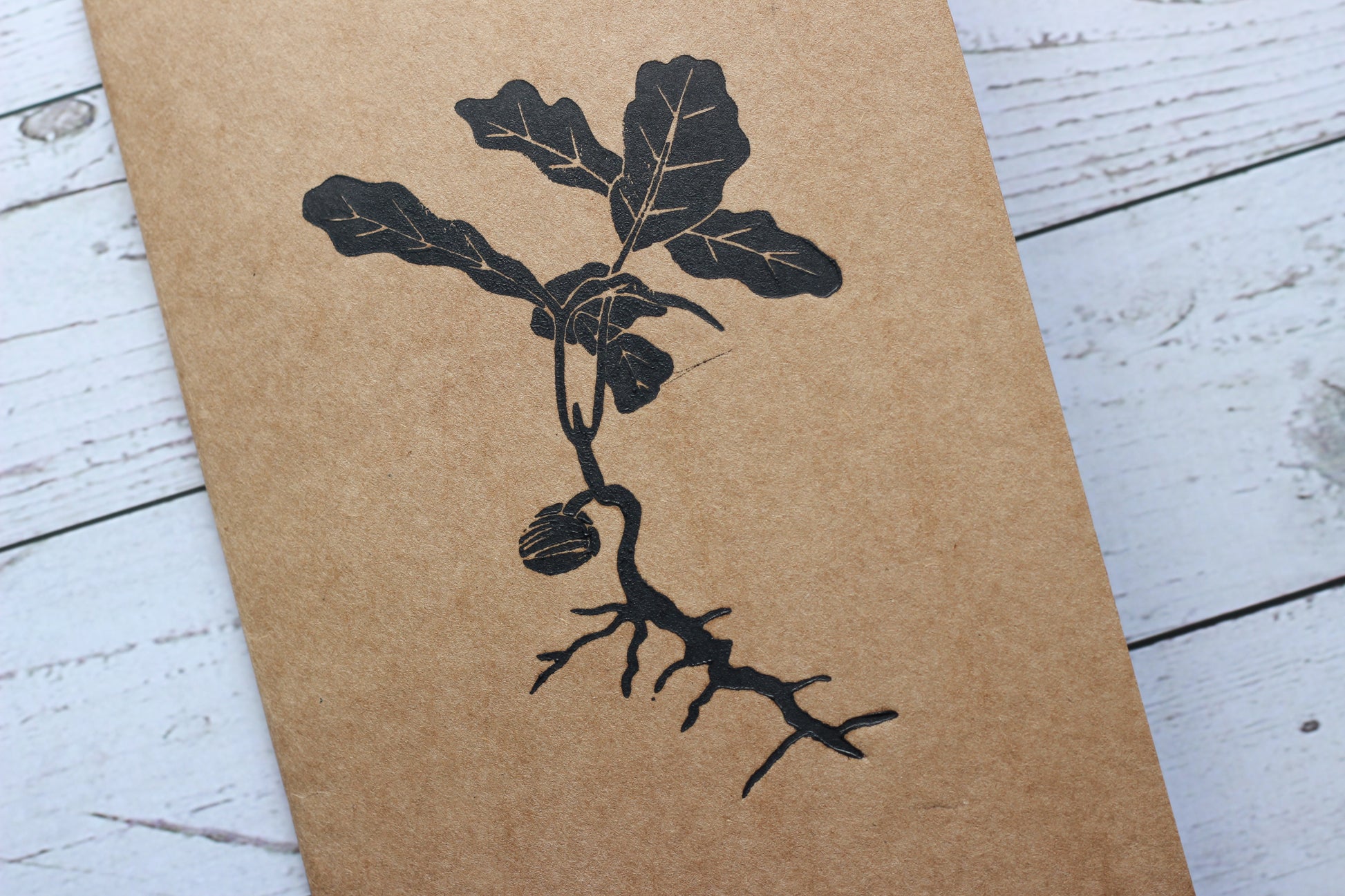 A lino printed sketchbook with a print of an oak sapling on the front