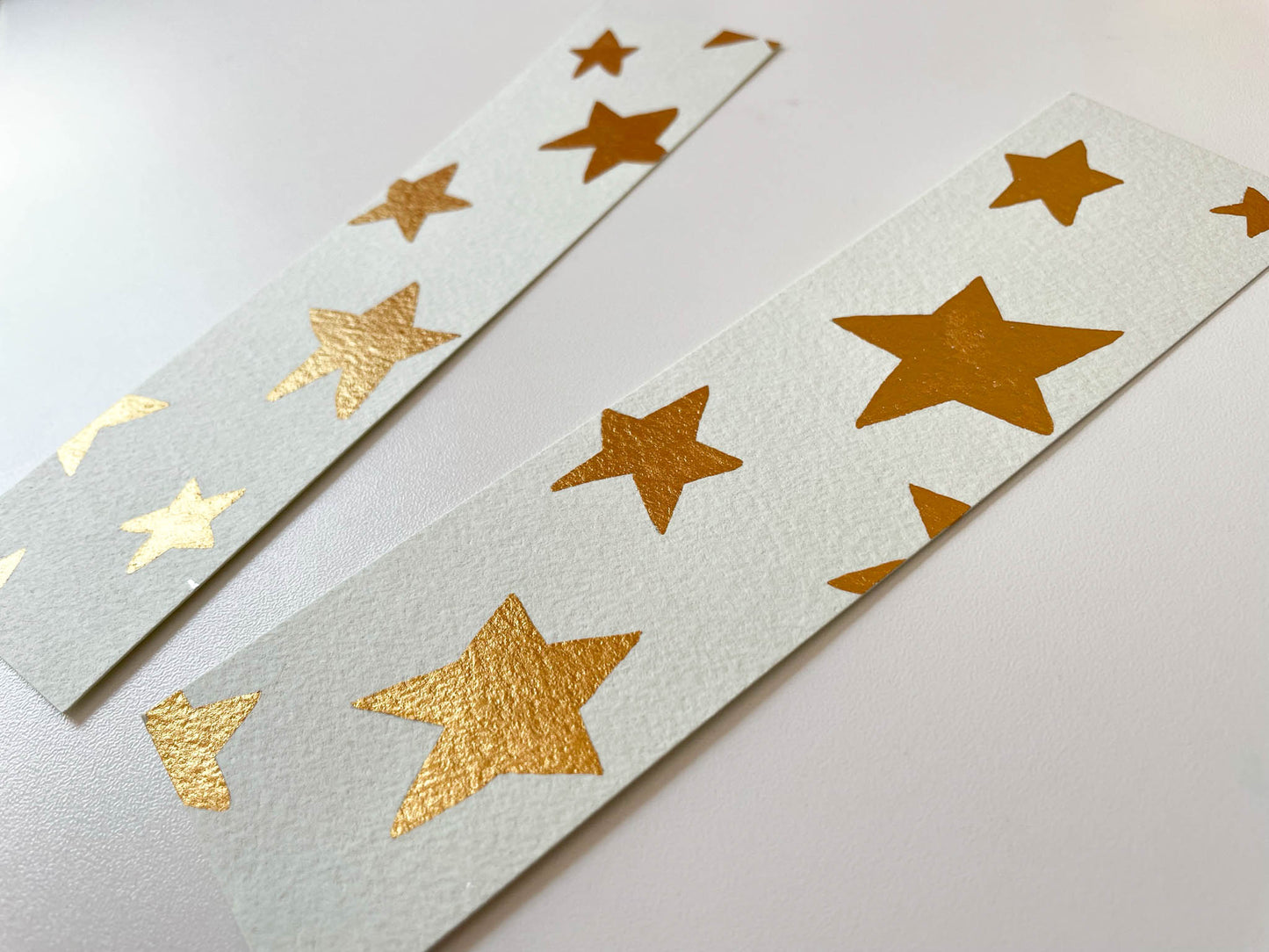 A photo of two hand painted watercolour bookmarks with gold metallic watercolour stars