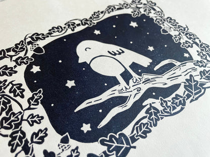 A small lino print of a robin on a tree surrounded by oak leaves and stars