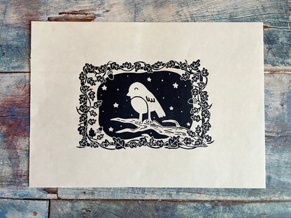 A small lino print of a robin on a tree surrounded by oak leaves and stars