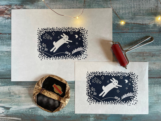 A navy blue lino print of a cute rabbit leaping through the air while surrounded by leaves, moon and stars