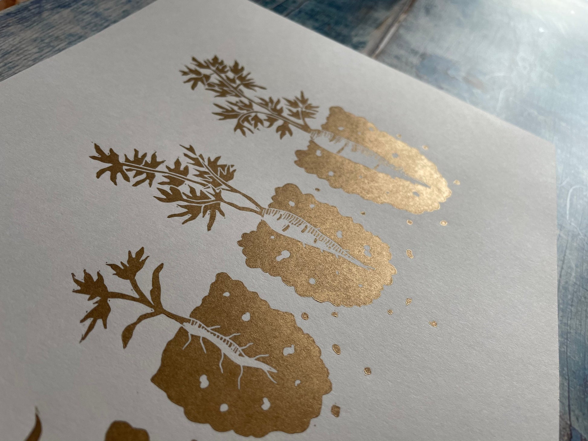 A lino print showing the different stages of a carrot growing from seedling to ready to pick in gold
