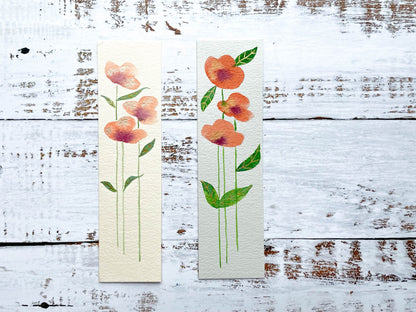 A photo of two hand painted watercolour bookmarks of orange flowers with gold embellishments