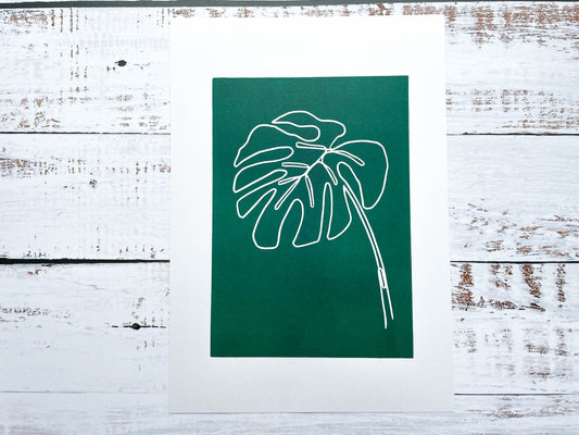 A continuous line lino print of a monstera plant leaf on a green background