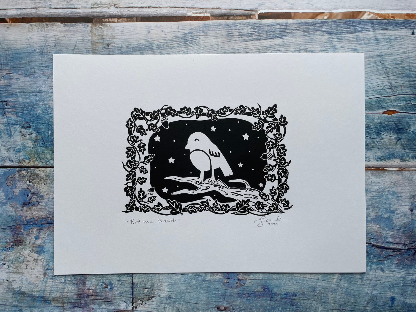 A small lino print of a robin on a tree surrounded by oak leaves and stars