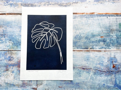 A continuous line lino print of a monstera plant leaf on a dark blue background