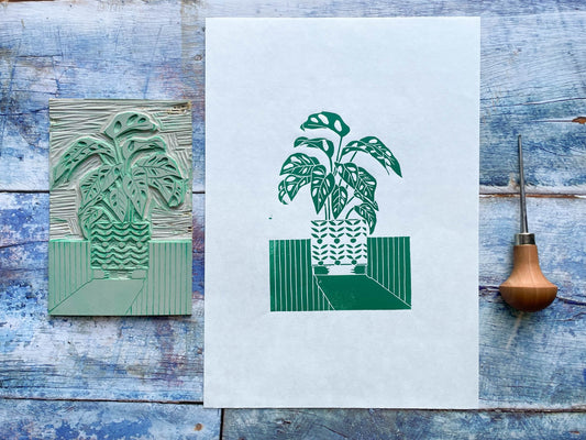 A green lino print of a monstera monkey plant in a patterned plant pot with a long shadow