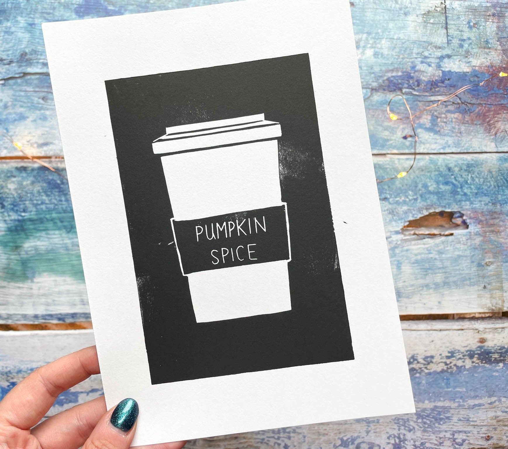 A simplistic lino print of a pumpkin spice latte in a takeout cup in black