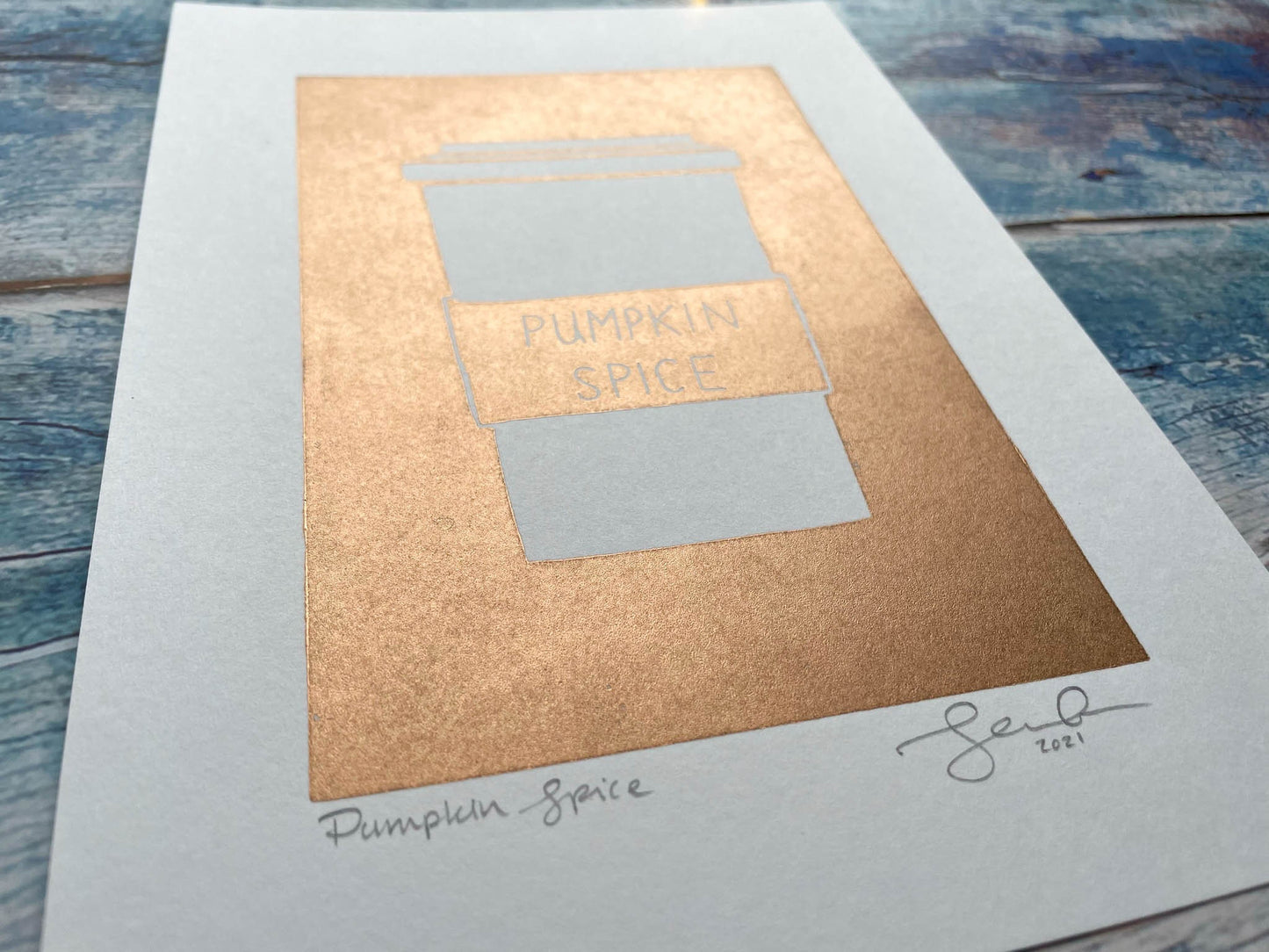 A simplistic lino print of a pumpkin spice latte in a takeout cup in copper