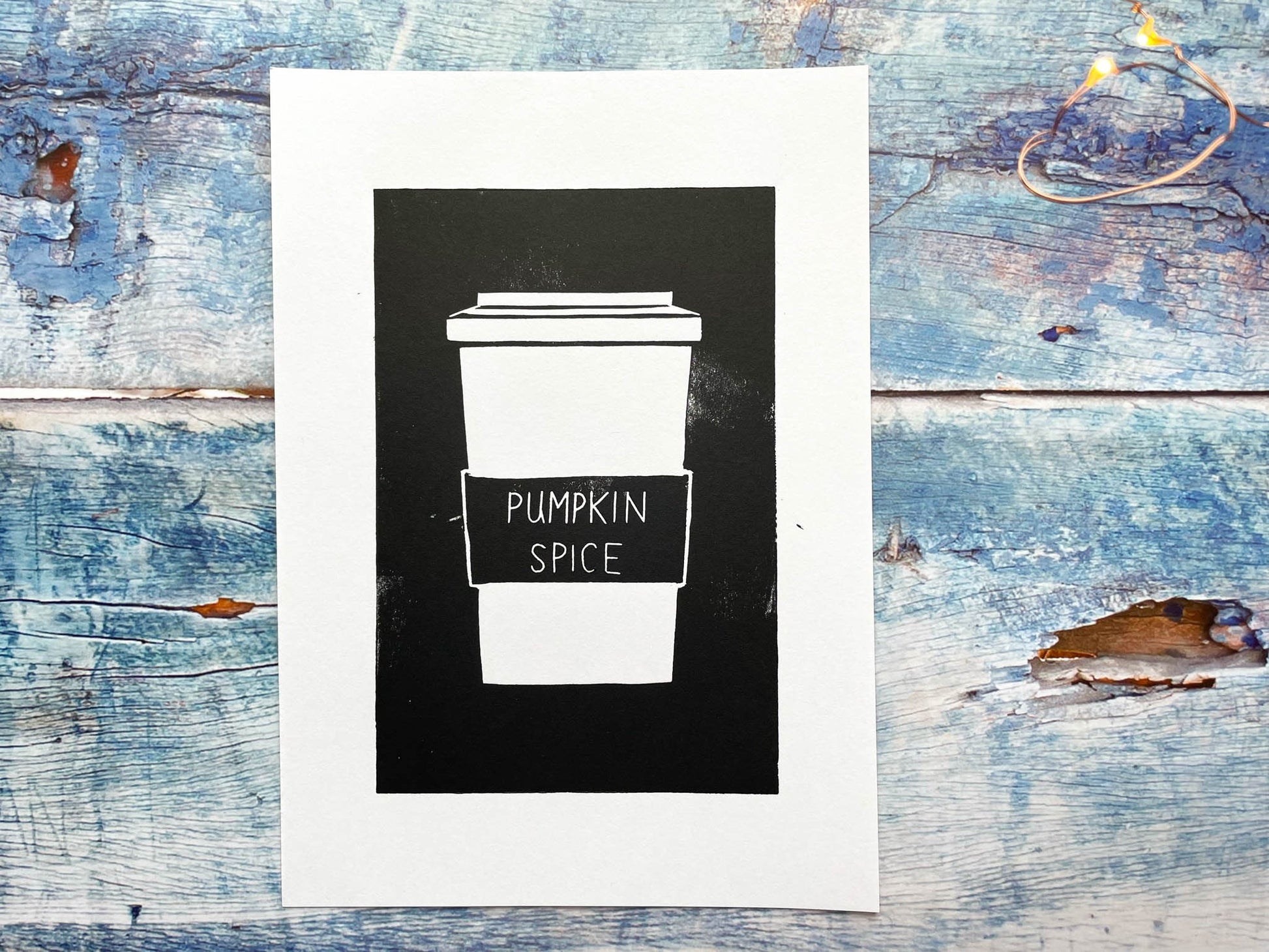 A simplistic lino print of a pumpkin spice latte in a takeout cup in black