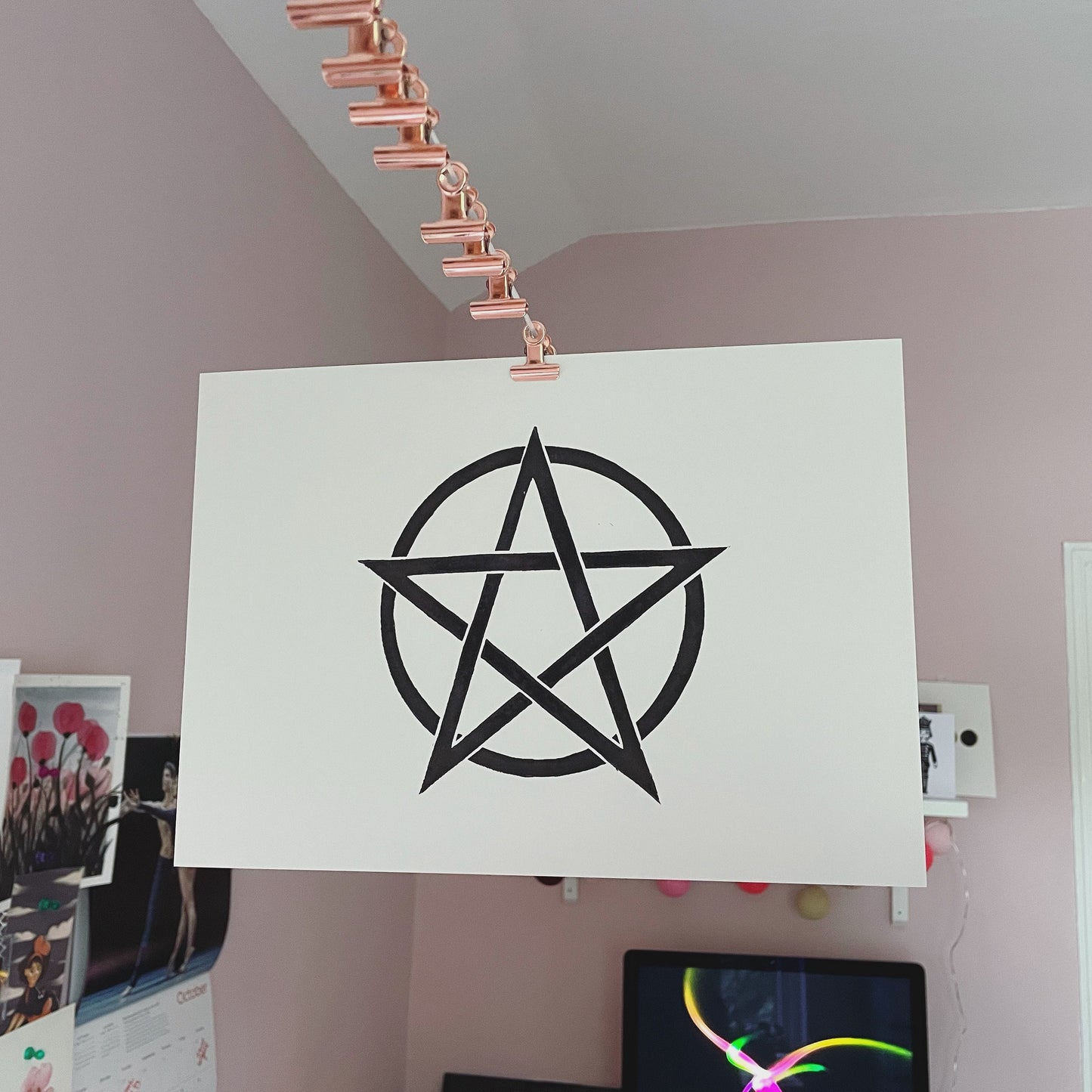 A simple black lino print of a pentagram in a circle hanging up to dry