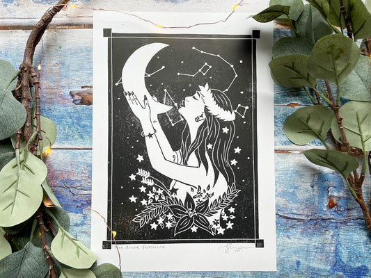 An A4 lino print of a women holding the moon up to her face with her hands, she's surrounded by stars and flowers