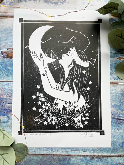 An A4 lino print of a women holding the moon up to her face with her hands, she's surrounded by stars and flowers